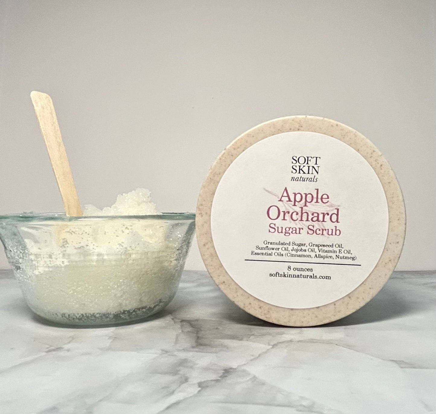 Apple Orchard Sugar Scrub with a bowl of scrub and a wooden spoon on a marble surface.