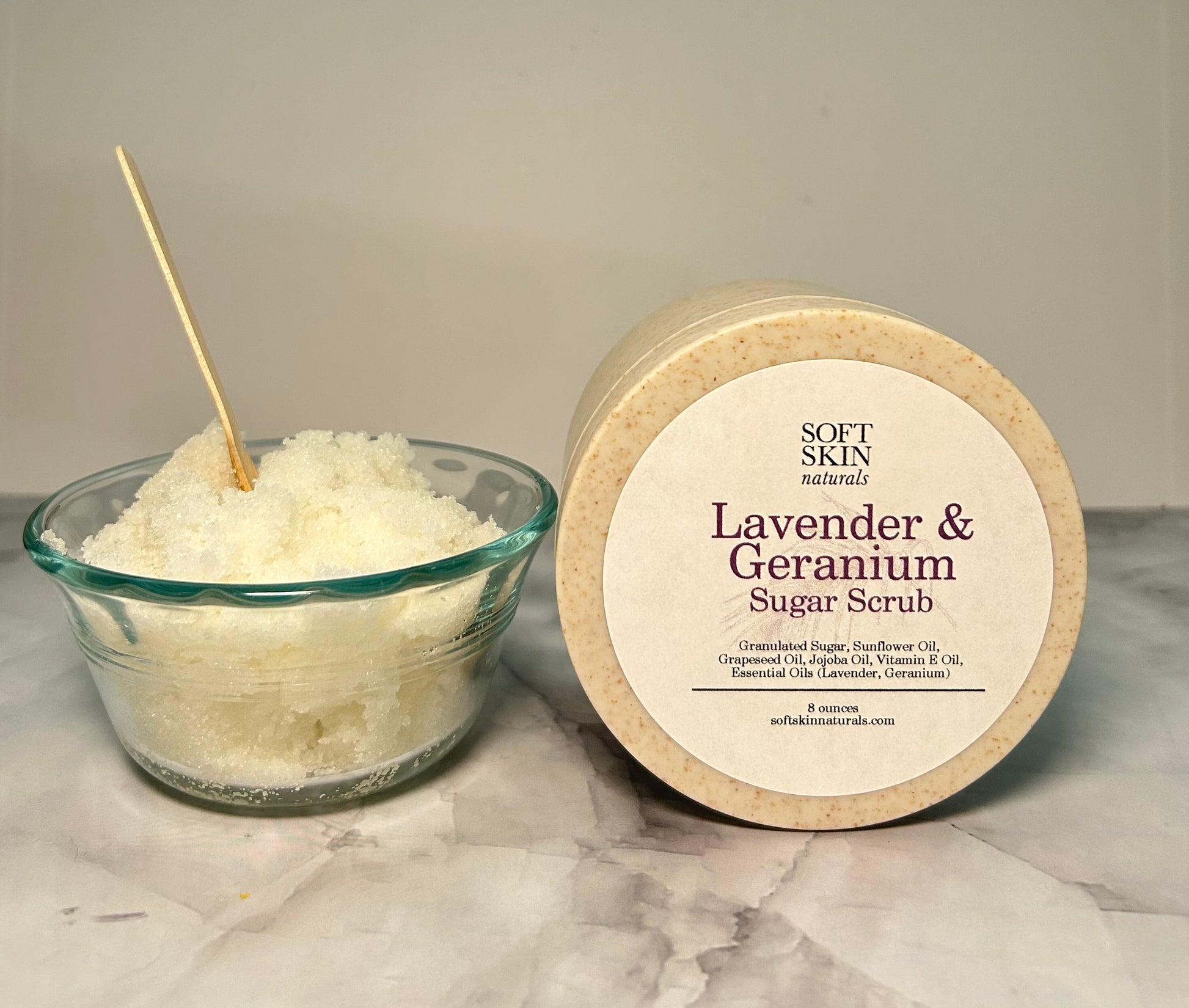 Lavender & Geranium sugar scrub in a container and bowl on a marble surface