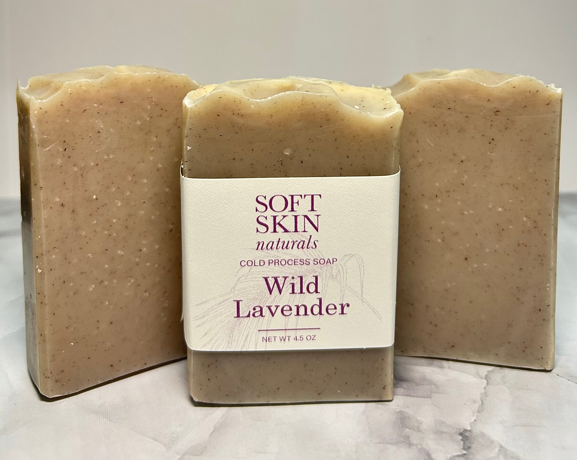 Three bars of Wild Lavender soap from Soft Skin Naturals on a marble surface.