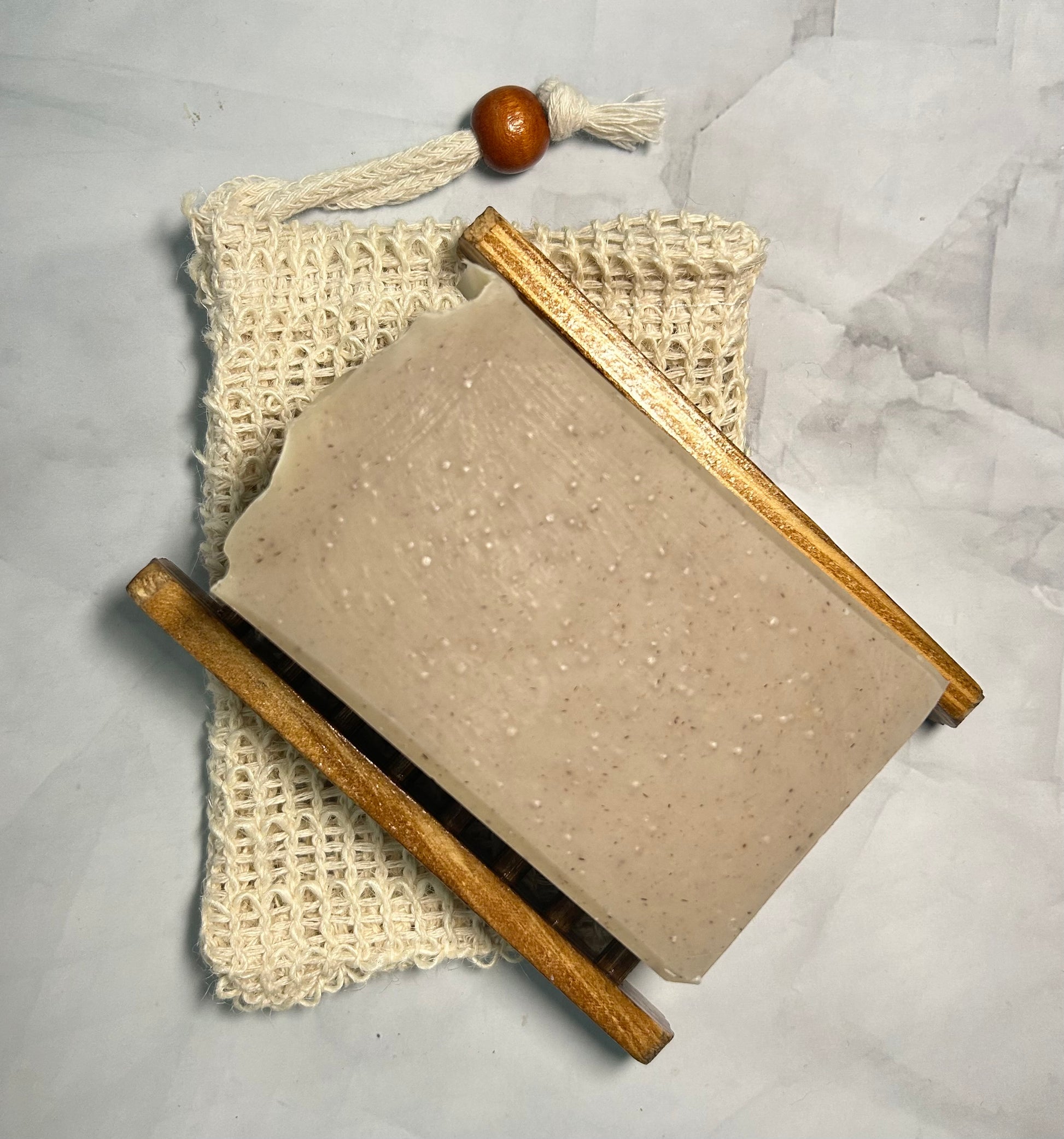 Bar of soap with a wooden handle and a mesh bag on a marble surface