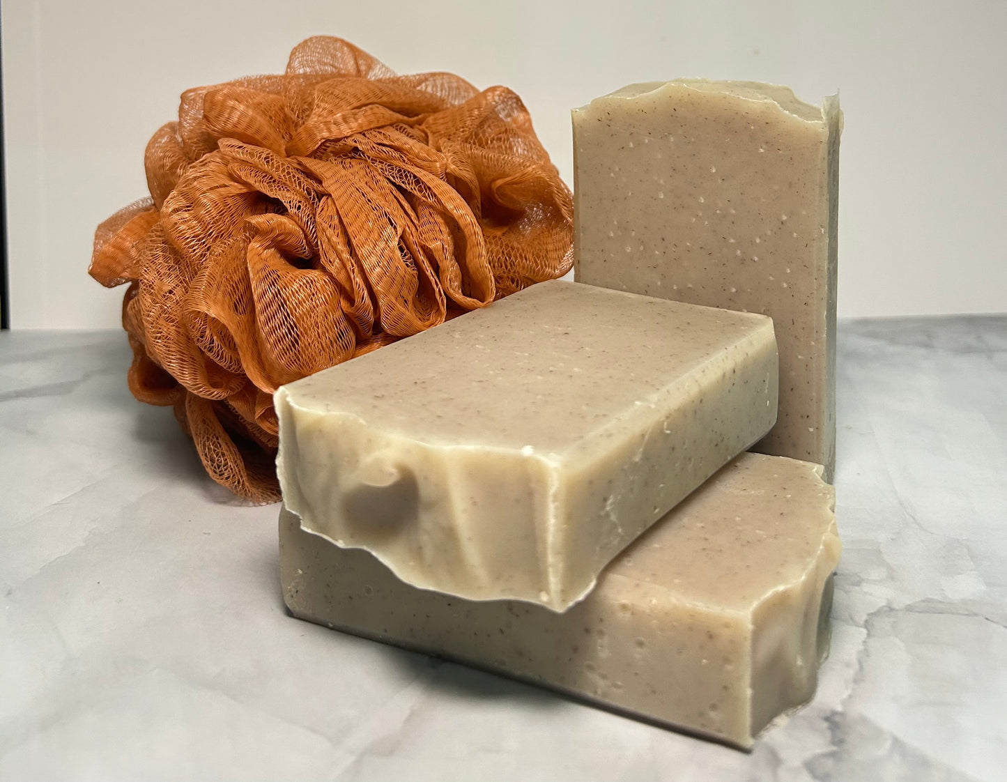 Three bars of soap and a brown loofah on a marble surface