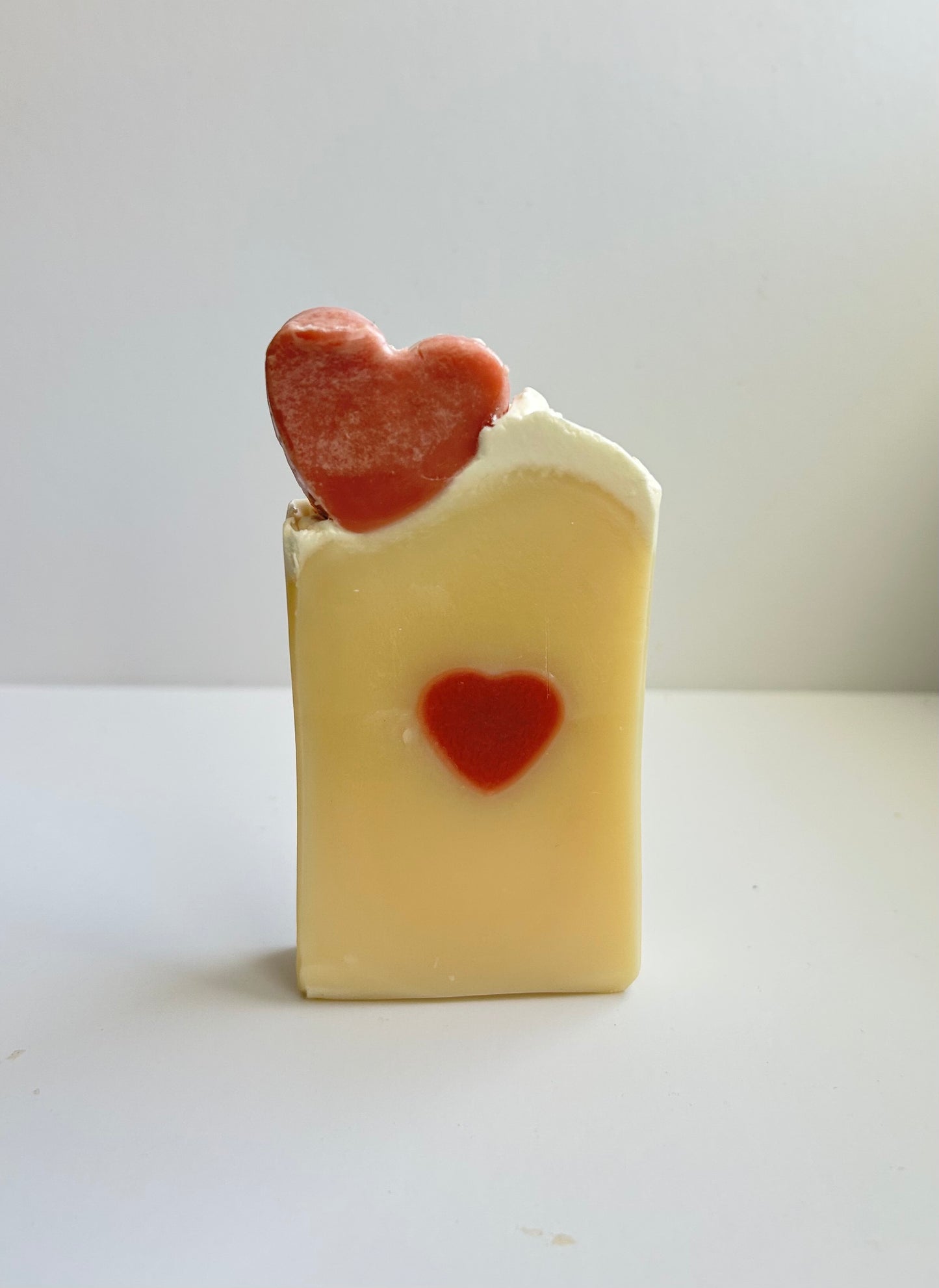 Bar of white soap with a red heart-shaped decoration on a light background