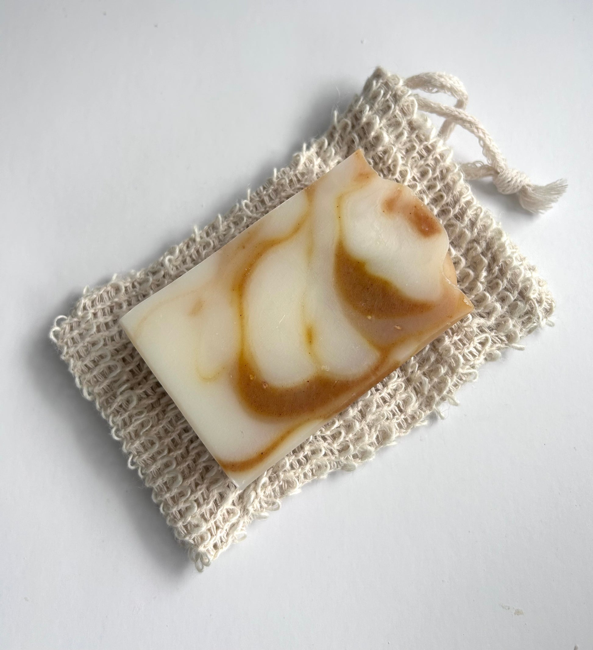 Bar of soap with brown swirls on a natural fiber soap bag against a white background