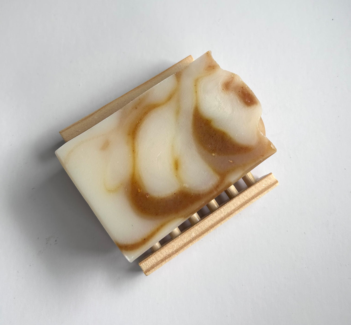 Bar of soap with brown and white swirls on a wooden soap dish against a light gray background