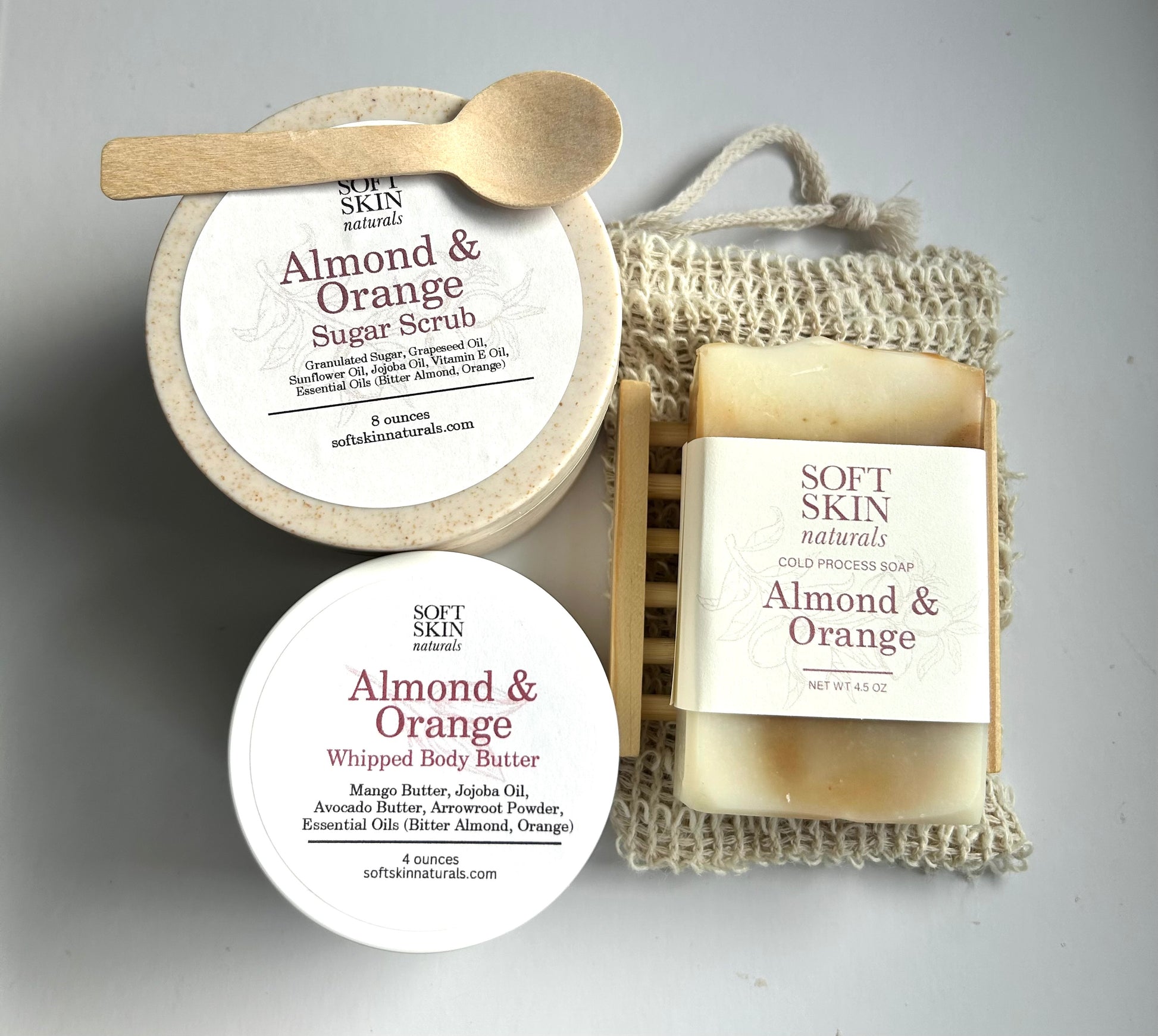 Collection of Soft Skin Almond & Orange products including a jar, soap, and body scrub on a neutral background.