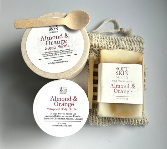 Collection of Soft Skin Almond & Orange products including a jar, soap, and body scrub on a neutral background.