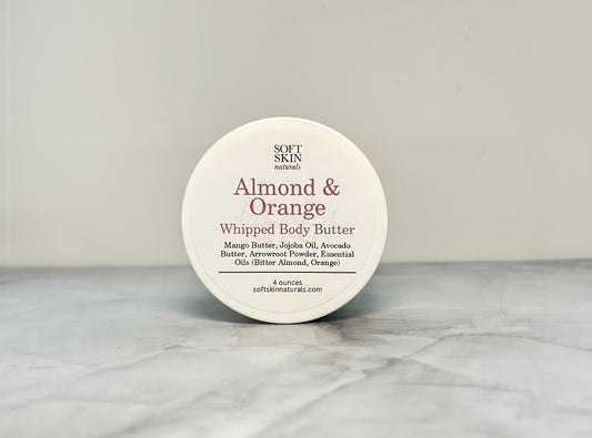Whipped body butter container labeled 'Almond & Orange' on a gray surface.