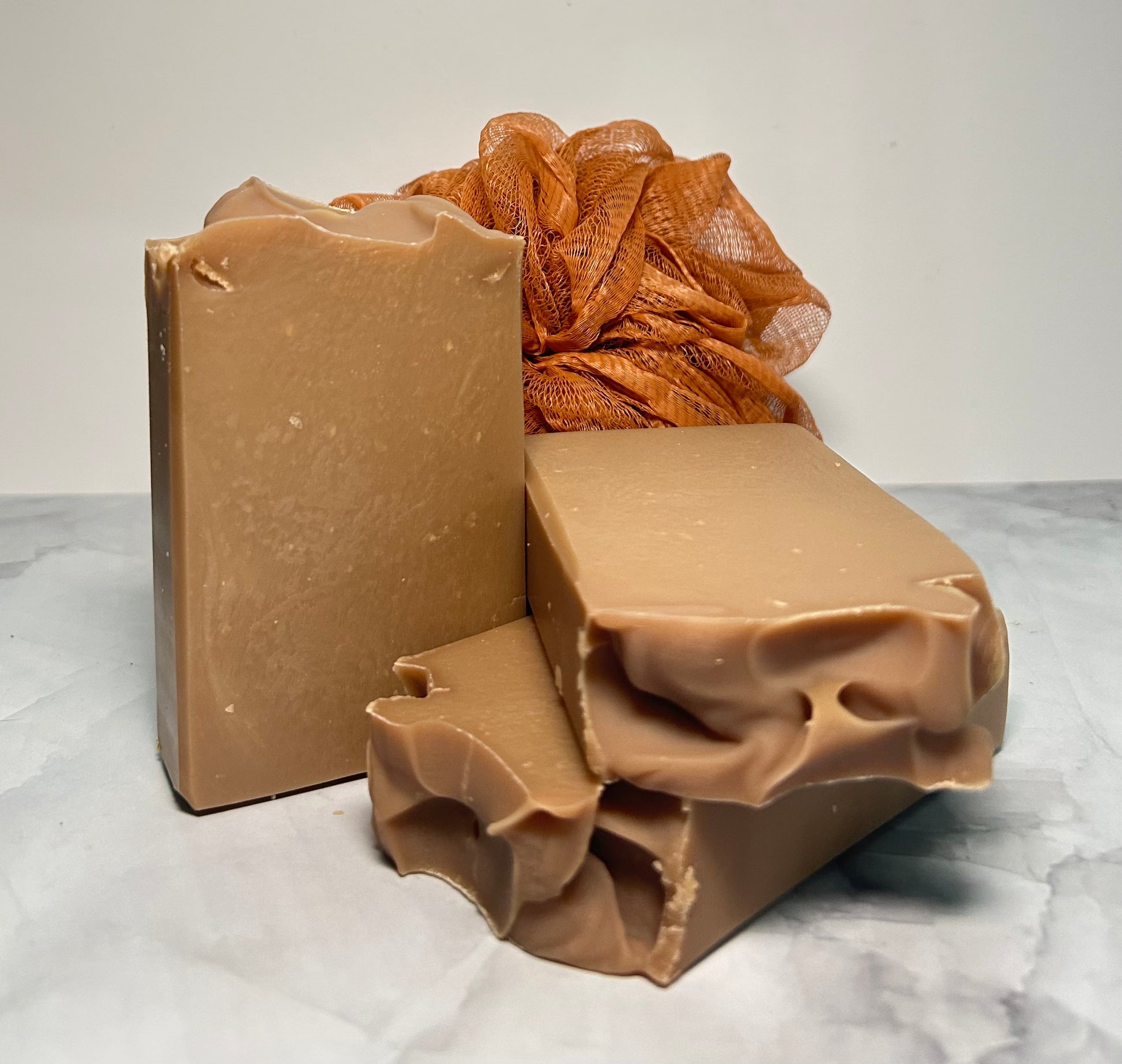 Two bars of brown soap and a loofah on a marble surface