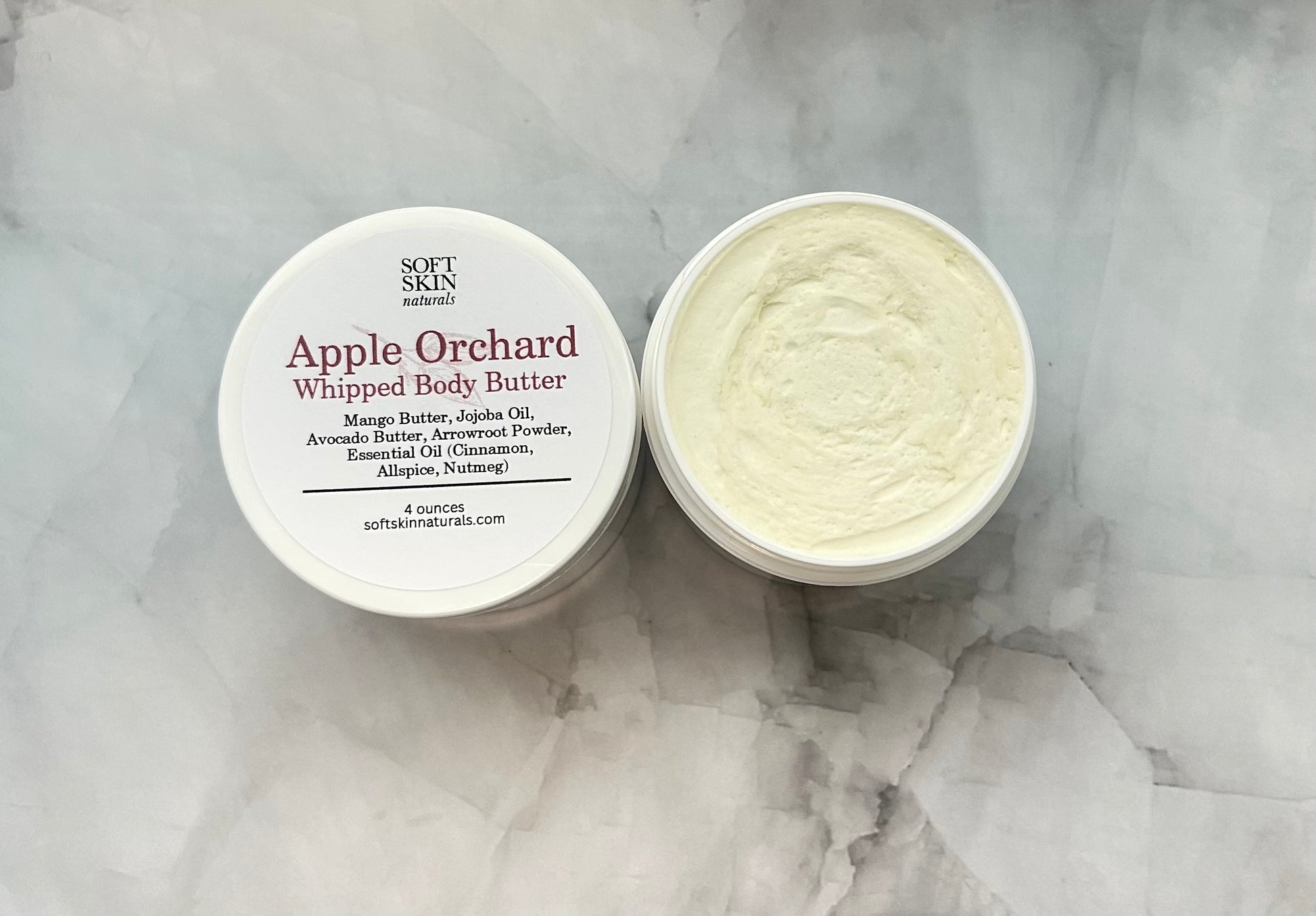 Opened jar of Apple Orchard whipped body butter sitting on a marbled table.