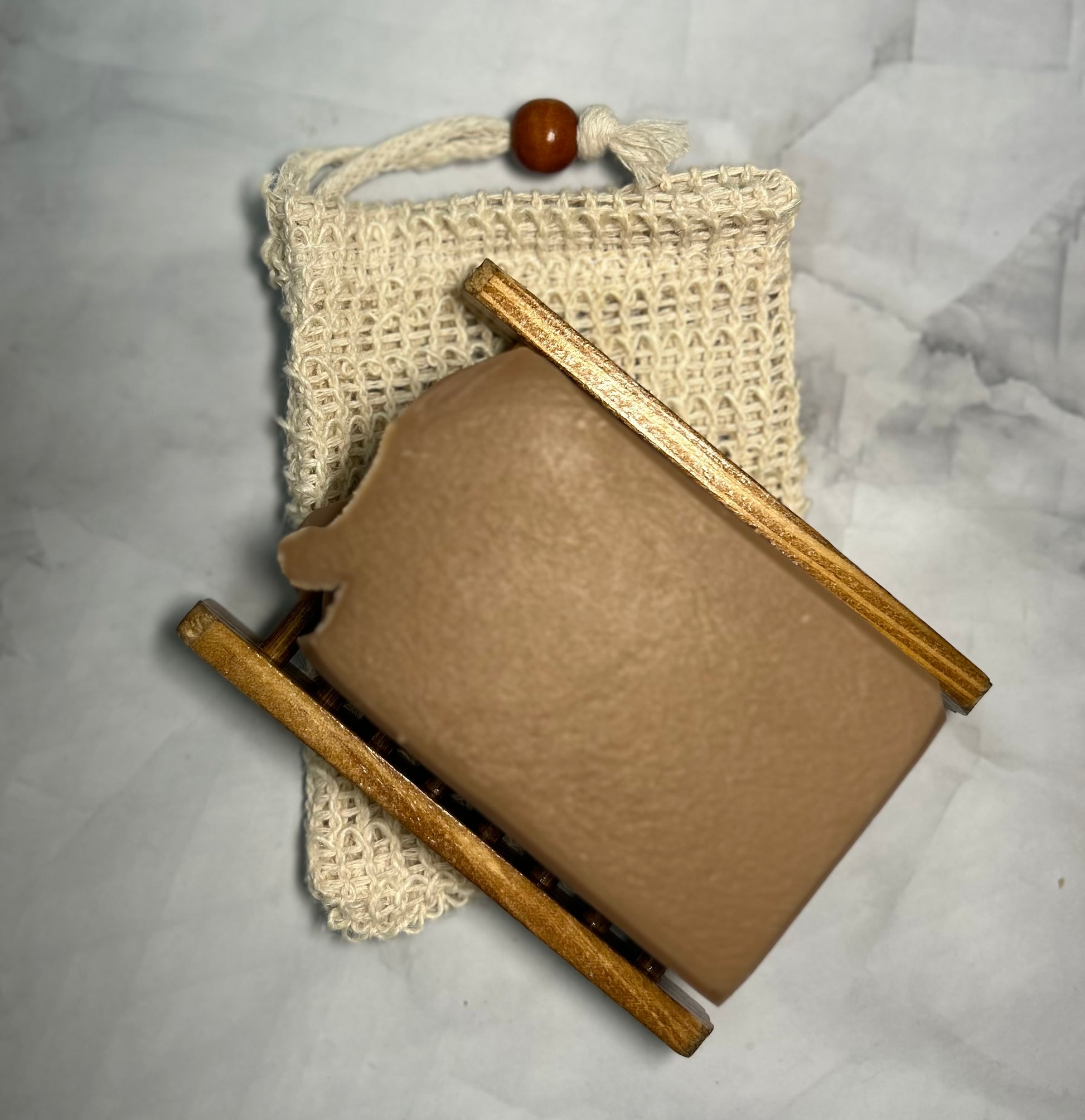 Brown soap bar with wooden soap holder and crochet bag on gray surface