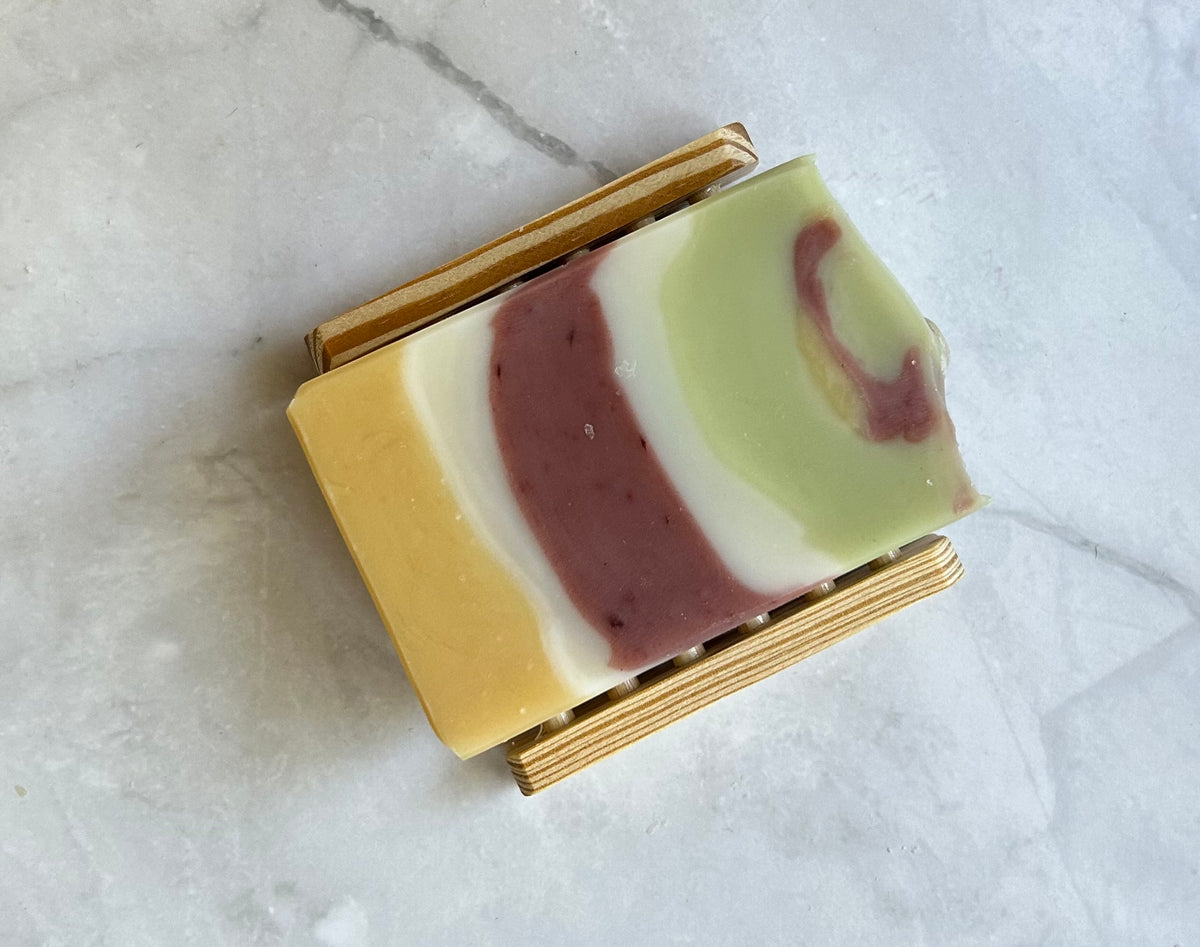 One bar of soap sitting on a wooden soap dish. 