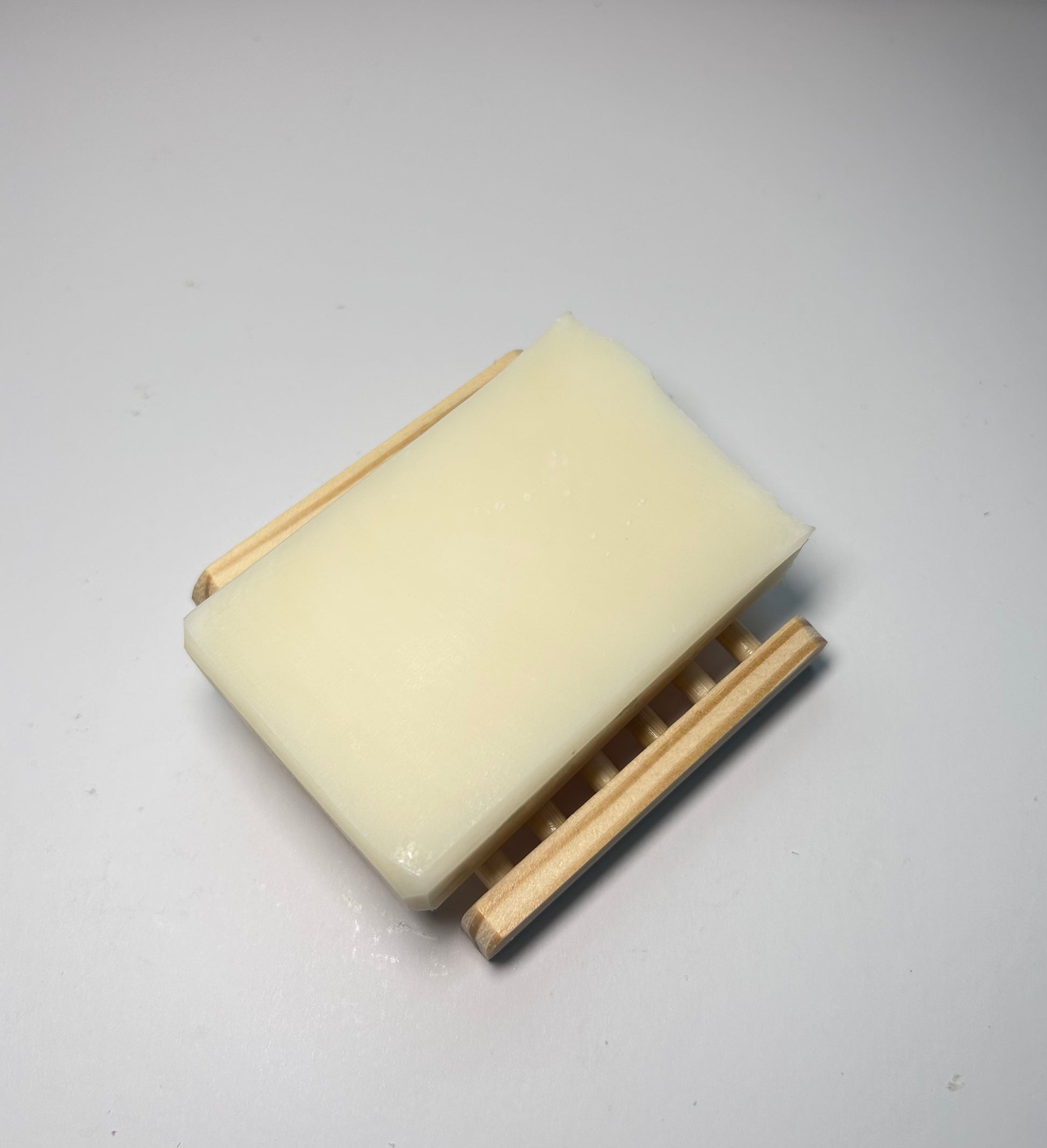 Rectangular cream-colored soap with wooden soap dish on a light gray background