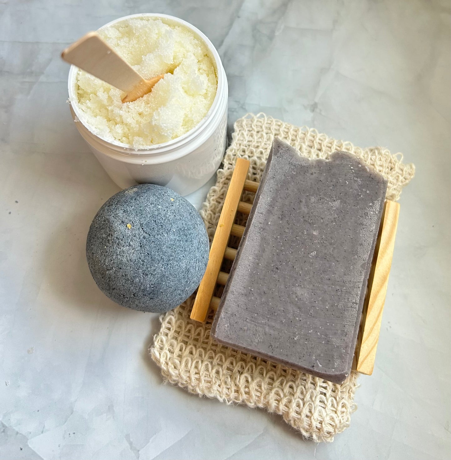 Bath bomb, charcoal soap bar, and scrubber on a marble surface