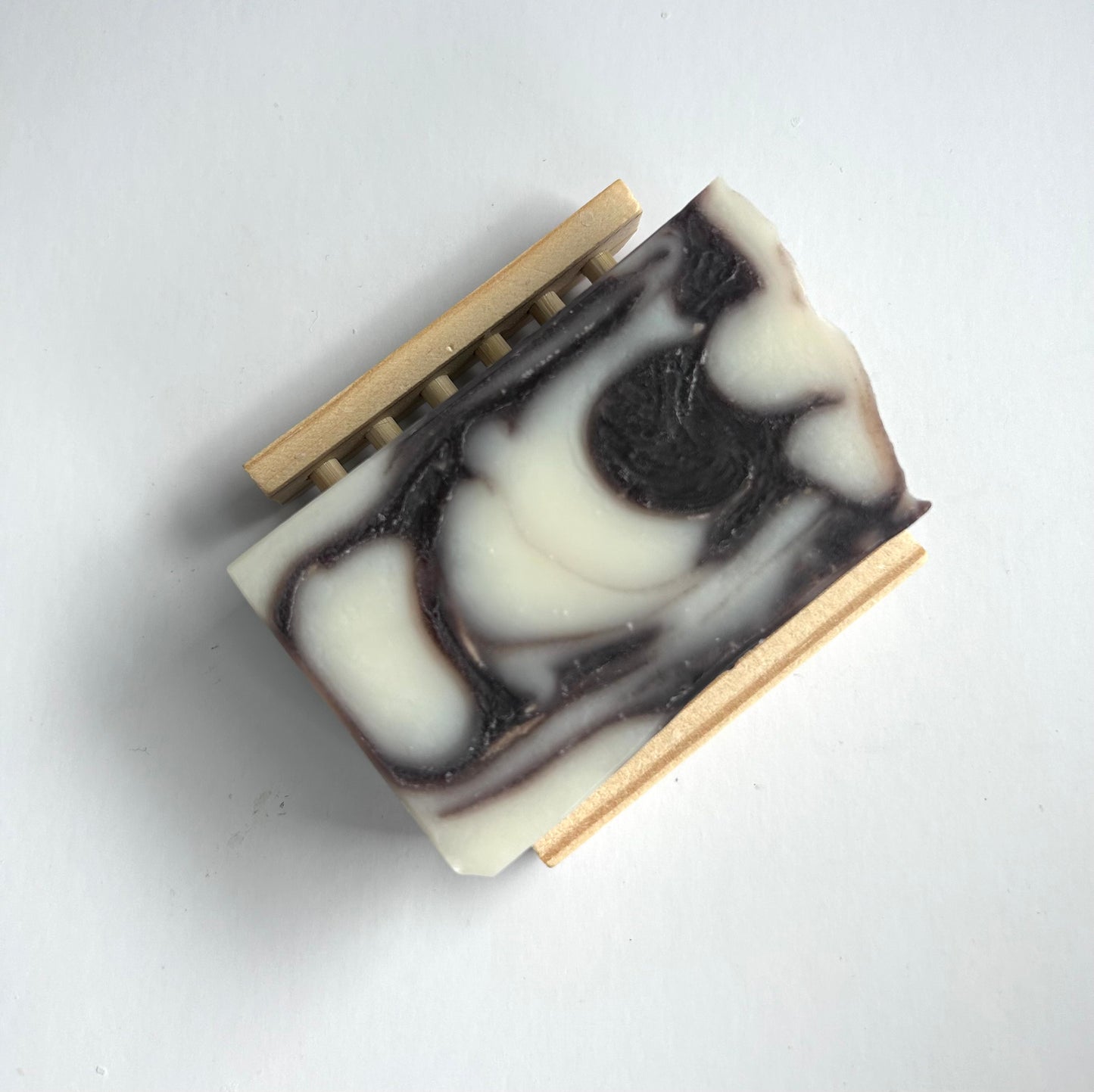 Bar of soap with black and white swirl pattern on a wooden soap dish against a light gray background