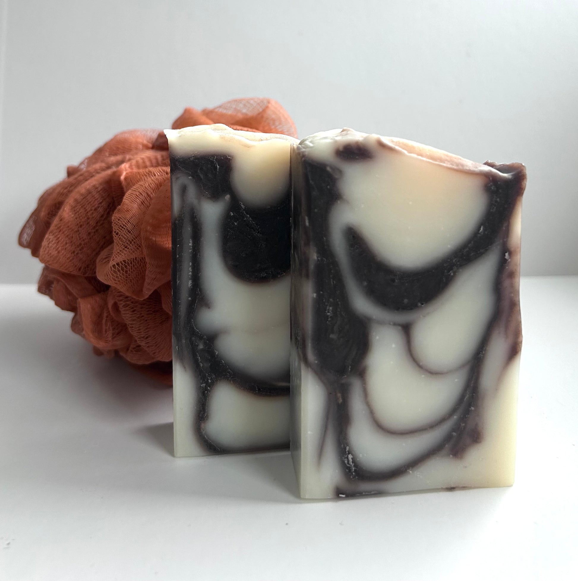 Two marbled soap bars with a brown loofah on a white background