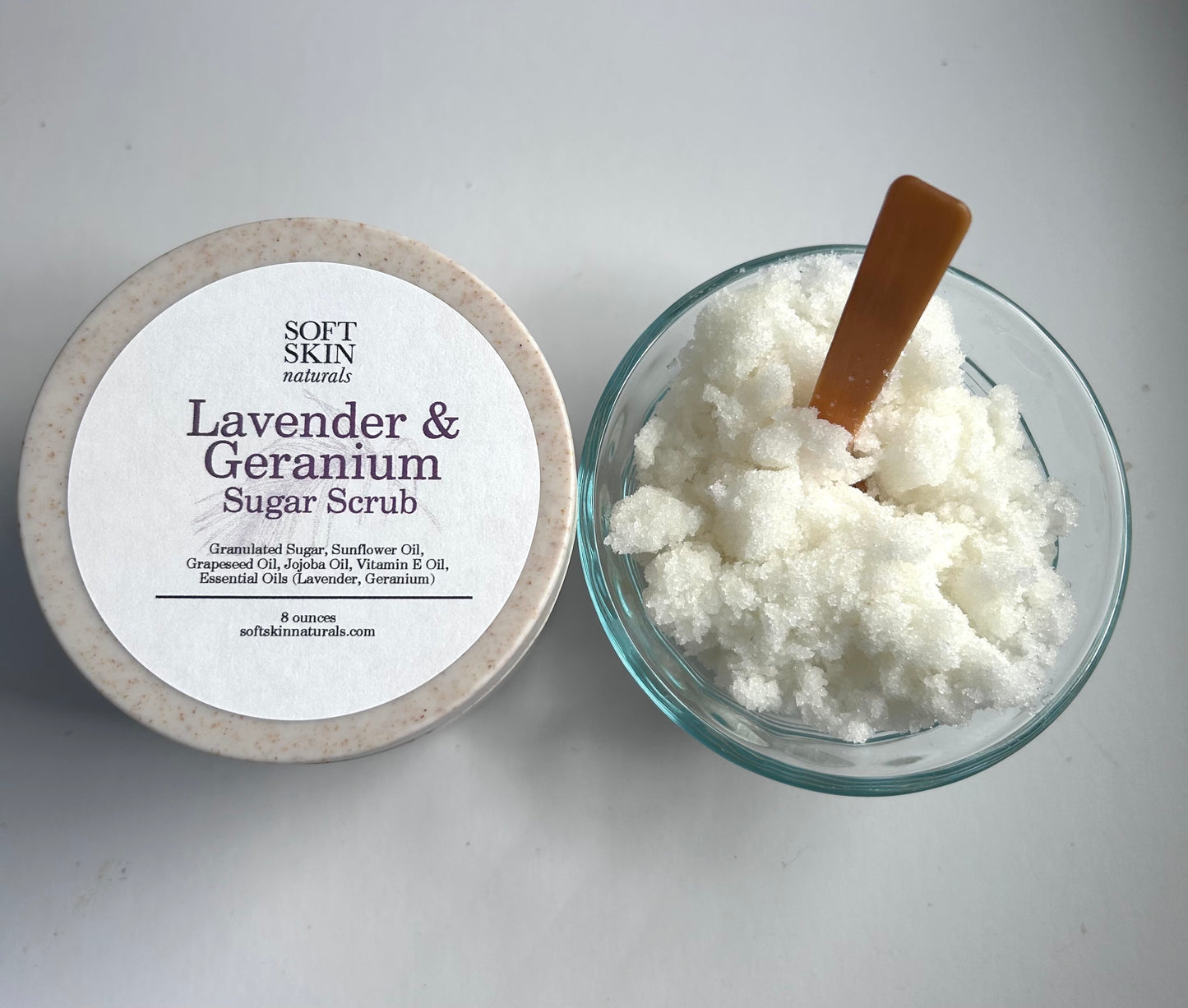 Lavender & Geranium sugar scrub with a wooden spoon on a white background