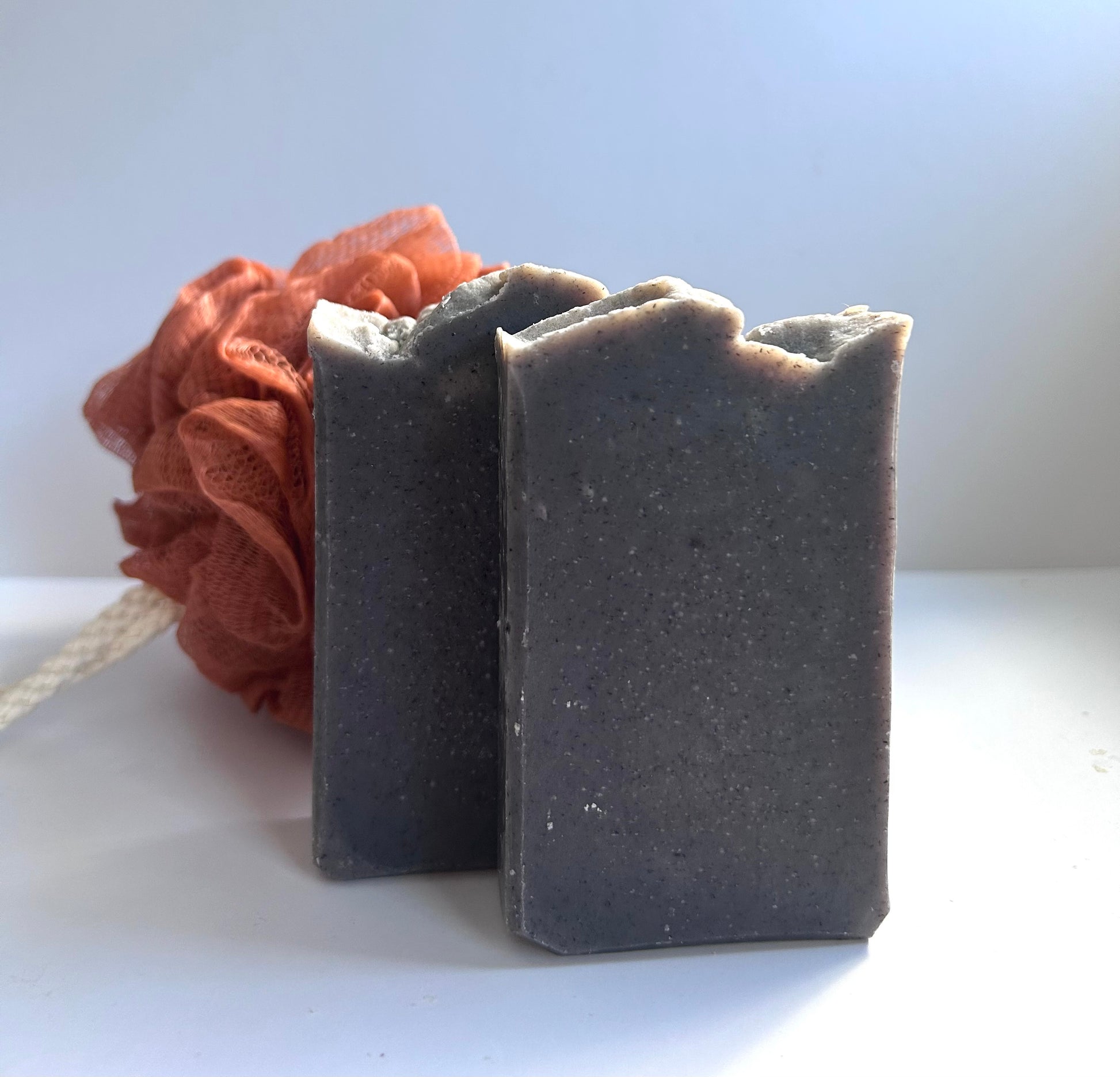 Two bars of dark soap with a brown loofah on a white background