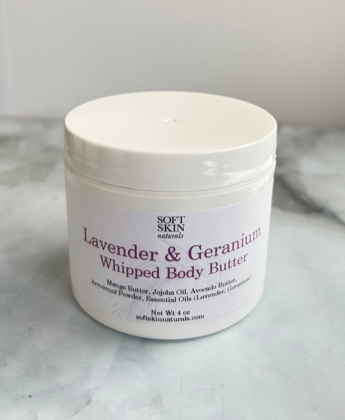 Jar of Lavender & Geranium Whipped Body Butter by Soft Skin Naturals on a marble surface.