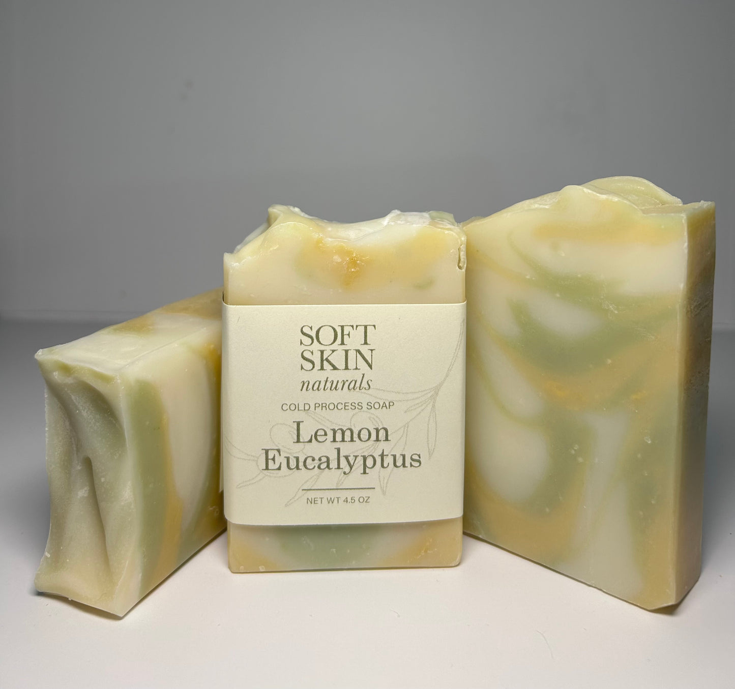 Three bars of lemon eucalyptus soap with a 'Soft Skin Naturals' label on a gray background