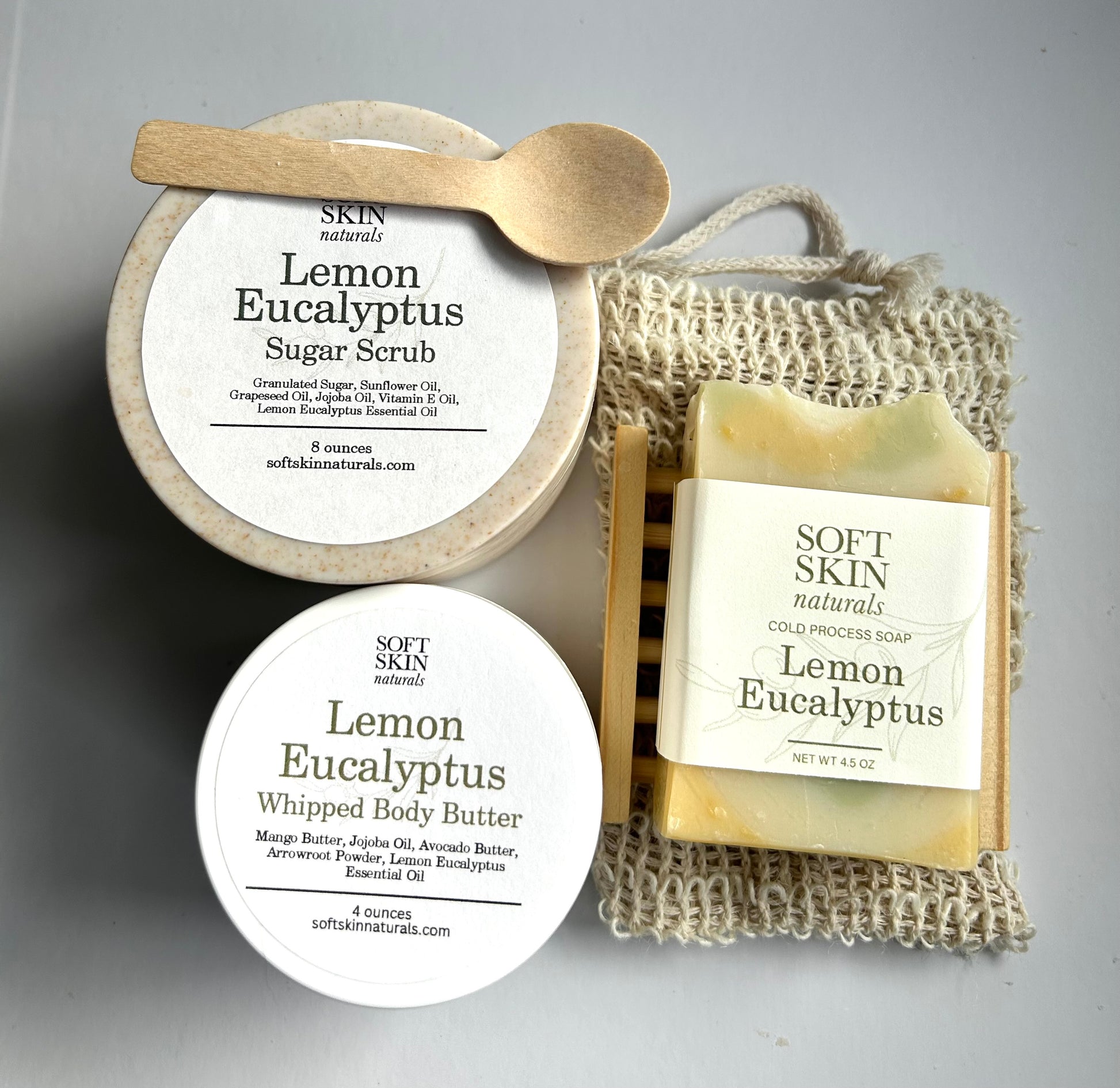 Collection of Soft Skin Lemon Eucalyptus products including sugar scrub, soap, and body butter on a gray background.