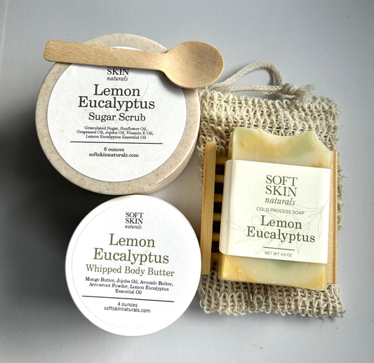 Collection of Soft Skin Lemon Eucalyptus products including sugar scrub, soap, and body butter on a gray background.