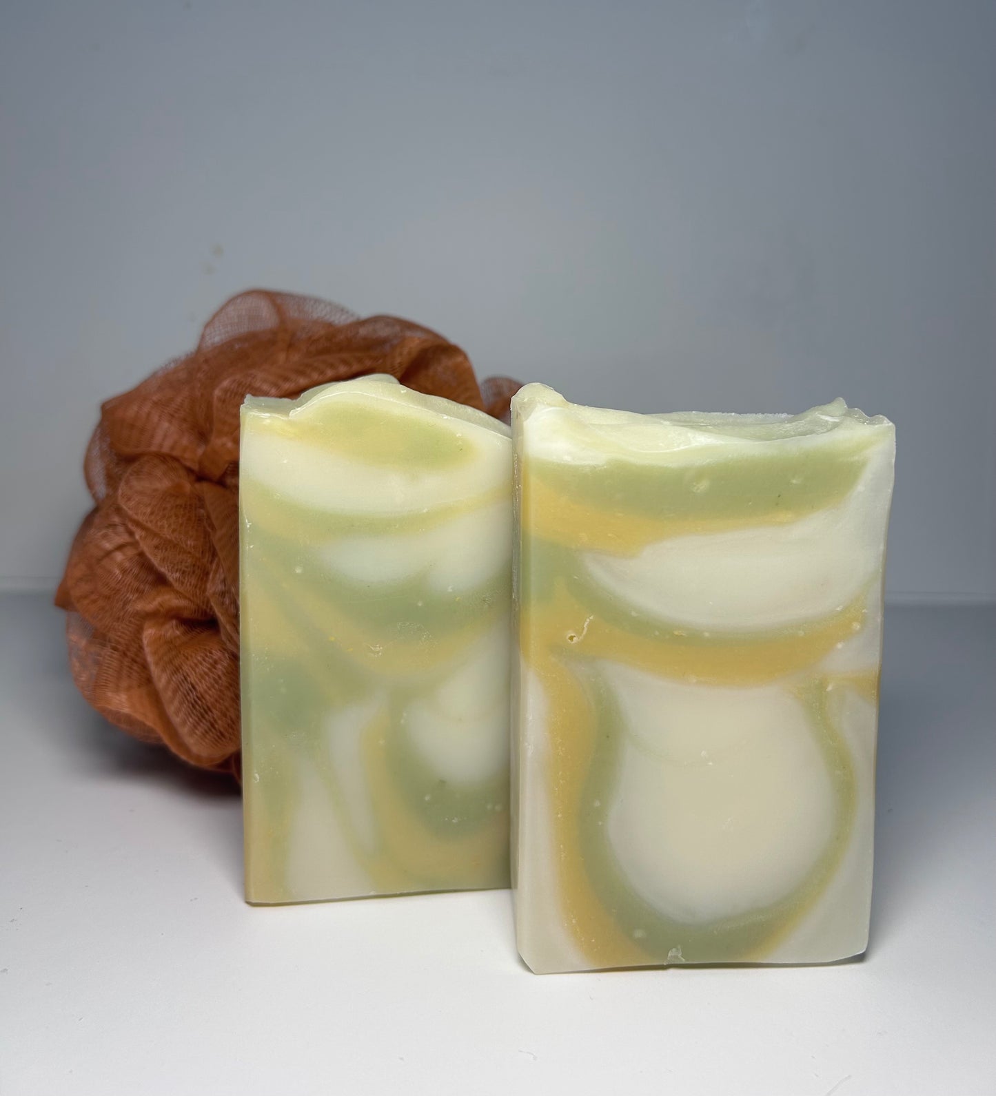 Two swirled soap bars with a brown loofah on a gray background
