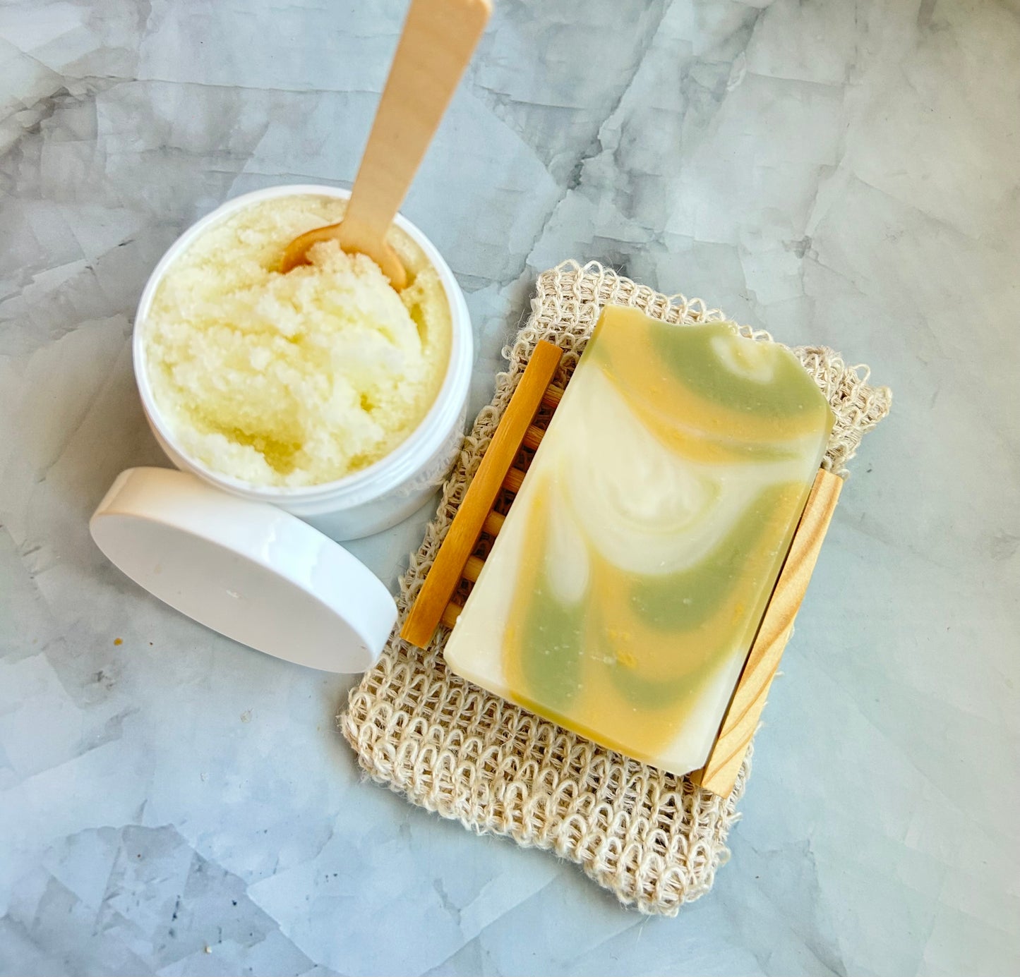 Bar of soap and container of scrub on a marble surface