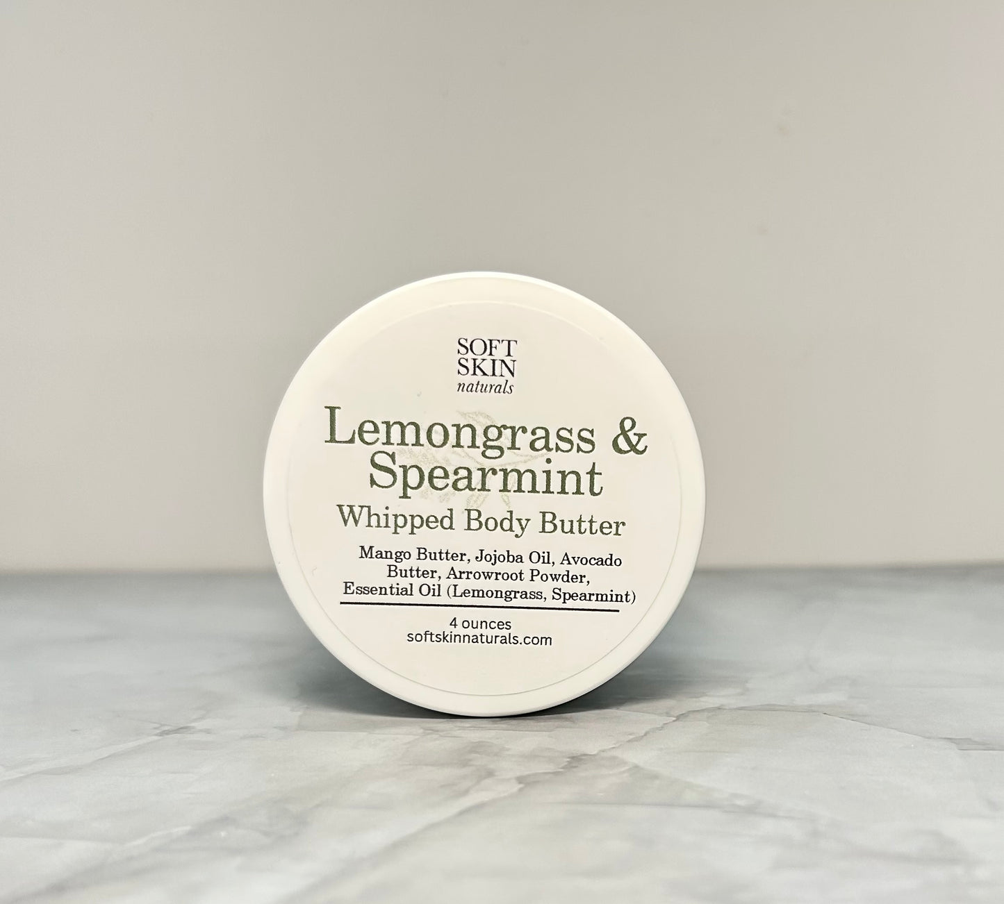 Round container of Soft Skin Naturals Lemongrass & Spearmint Whipped Body Butter on a marble surface.
