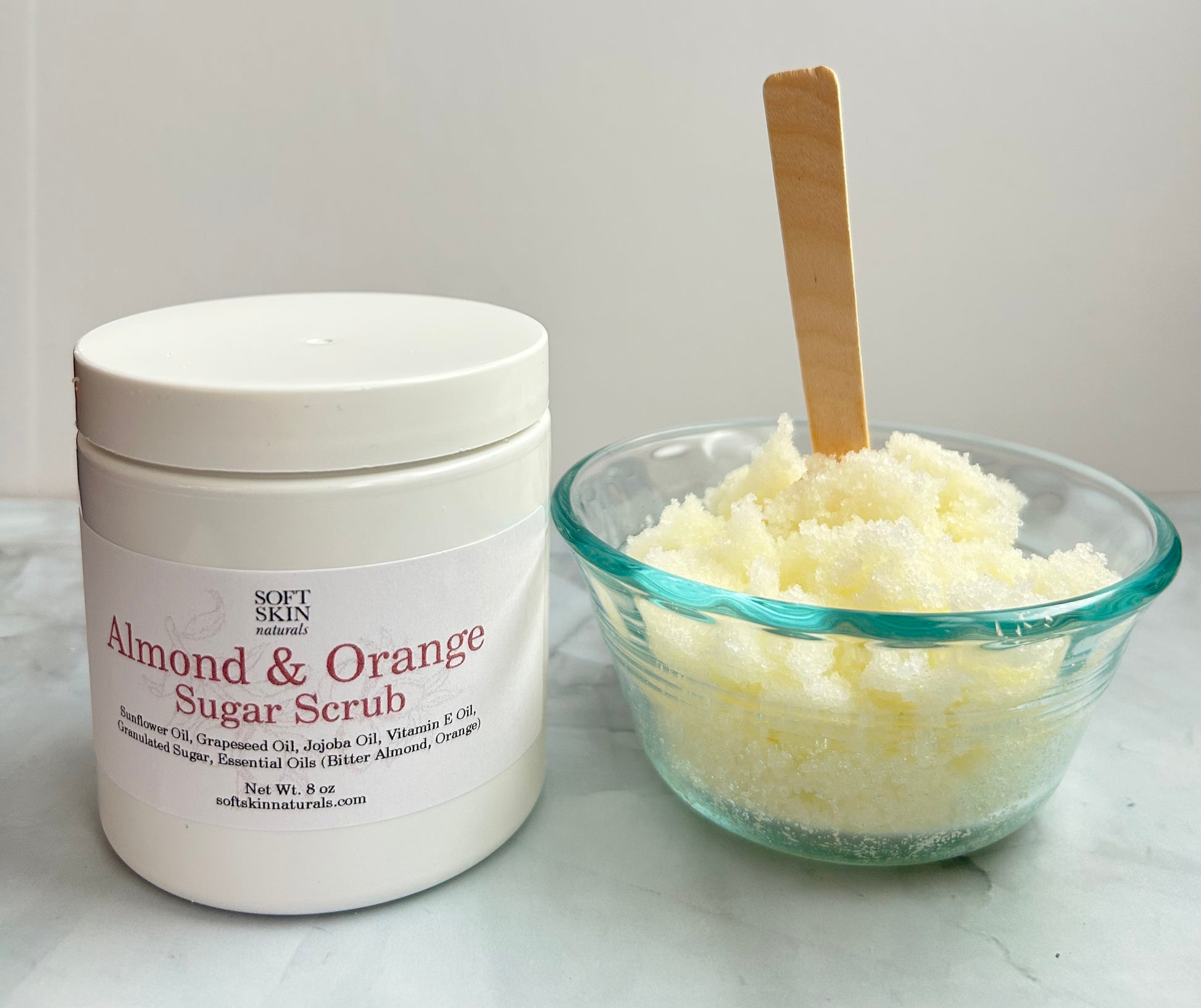 Almond & Orange Sugar Scrub container with a glass bowl of scrub on a white surface