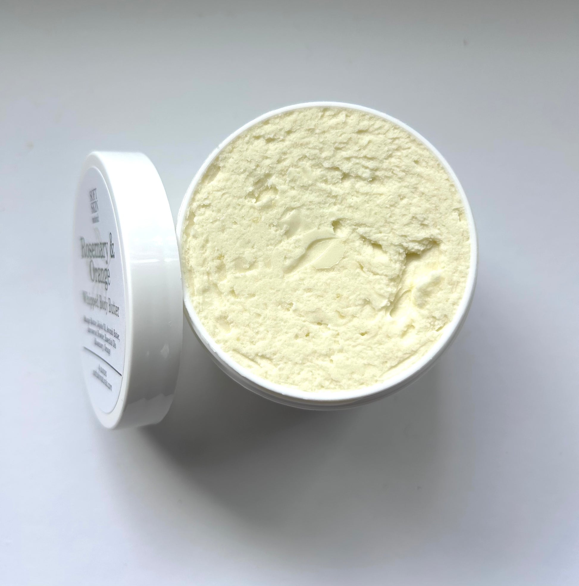 White container of body butter with a white lid on a light gray background