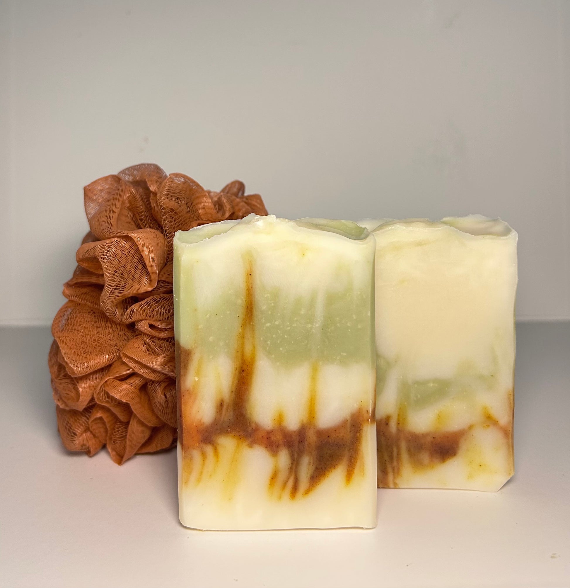 Two bars of soap with a brown scrubber on a light gray background