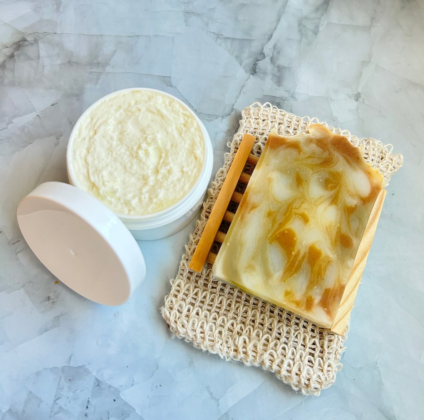 Bar of soap and a container of body butter on a marble surface