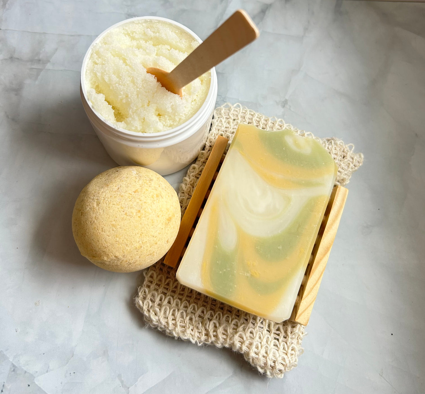 Bath products including a jar of bath butter, a bar of soap, and a loofah on a marble surface.