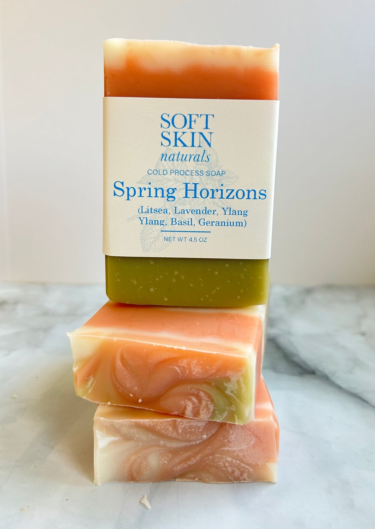 Three bars of soap stacked on a marble surface with 'Soft Skin Naturals' packaging.