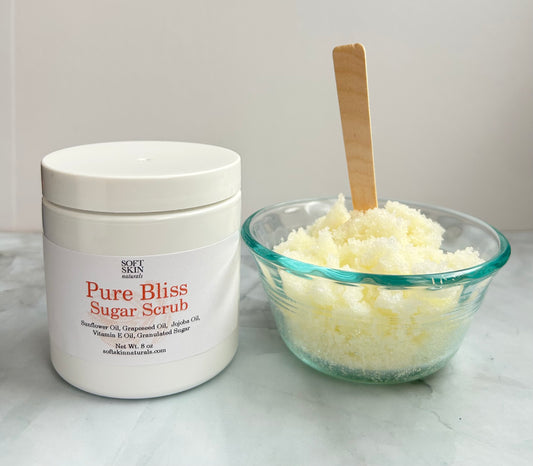 Jar of Soft Skin Pure Bliss Sugar Scrub next to a glass bowl filled with sugar scrub on a white surface.
