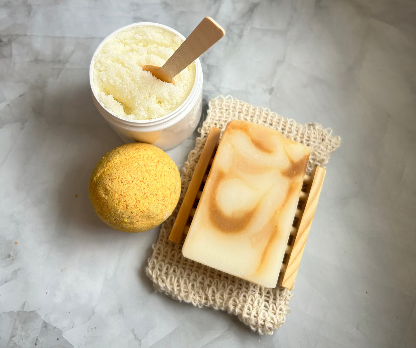 Bar of soap, loofah, and jar of bath scrub on a marble surface