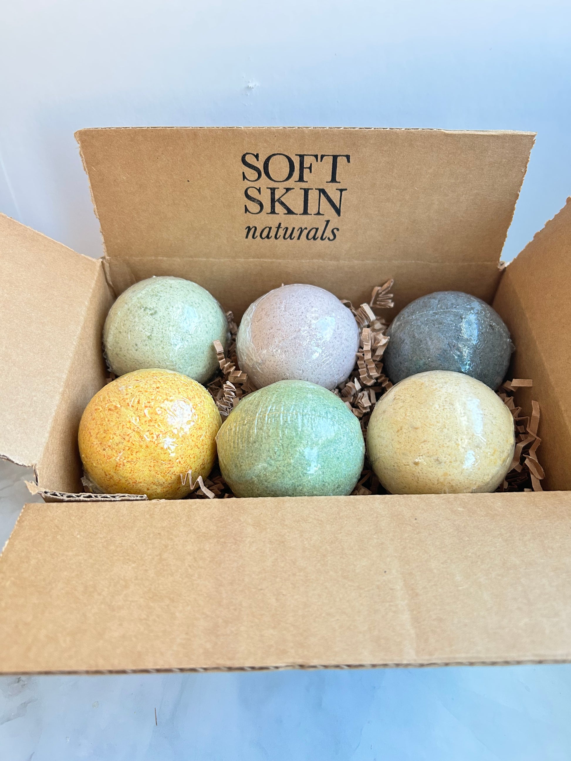 Box of bath bombs with 'Soft Skin Naturals' branding on a light blue background