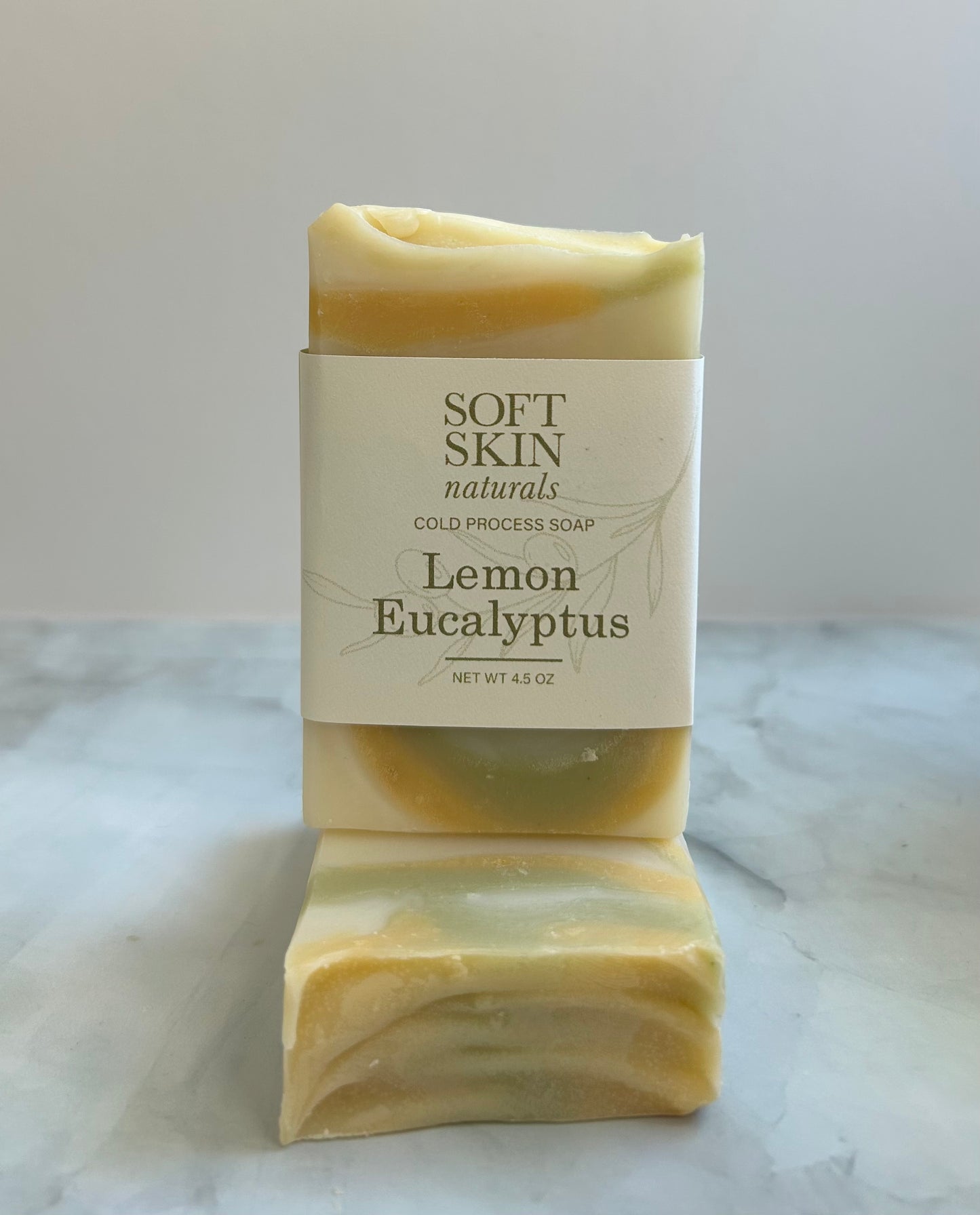 Two bars of lemon eucalyptus soap with a 'Soft Skin Naturals' label on a marble surface.